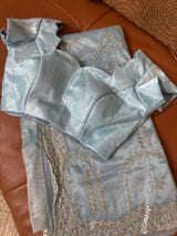 Vasundhara Fashions blue tissue saree with intricate gold embroidery and matching blouse piece on leather surface