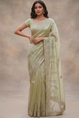 Model wearing a Vasundhara Fashions light green tissue saree with intricate silver embroidery and scalloped borders.