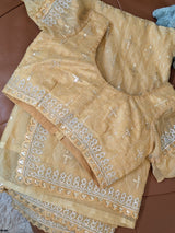 Vasundhara Fashions mustard organza saree with matching stitched blouse featuring intricate silver sequin embroidery.
