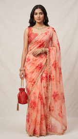 Vasundhara Fashions peach organza saree with red floral print, gold lace border, and matching sleeveless blouse.