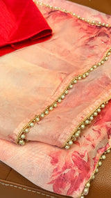 Vasundhara Fashions pink floral organza saree with delicate pearl-embellished gold border and red blouse piece