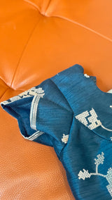 Vasundhara Fashions teal green organza saree with intricate silver thread embroidery on a textured orange surface