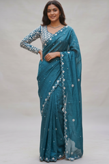 Vasundhara Fashions teal Russian silk saree with intricate white floral embroidery and a matching long-sleeve blouse.
